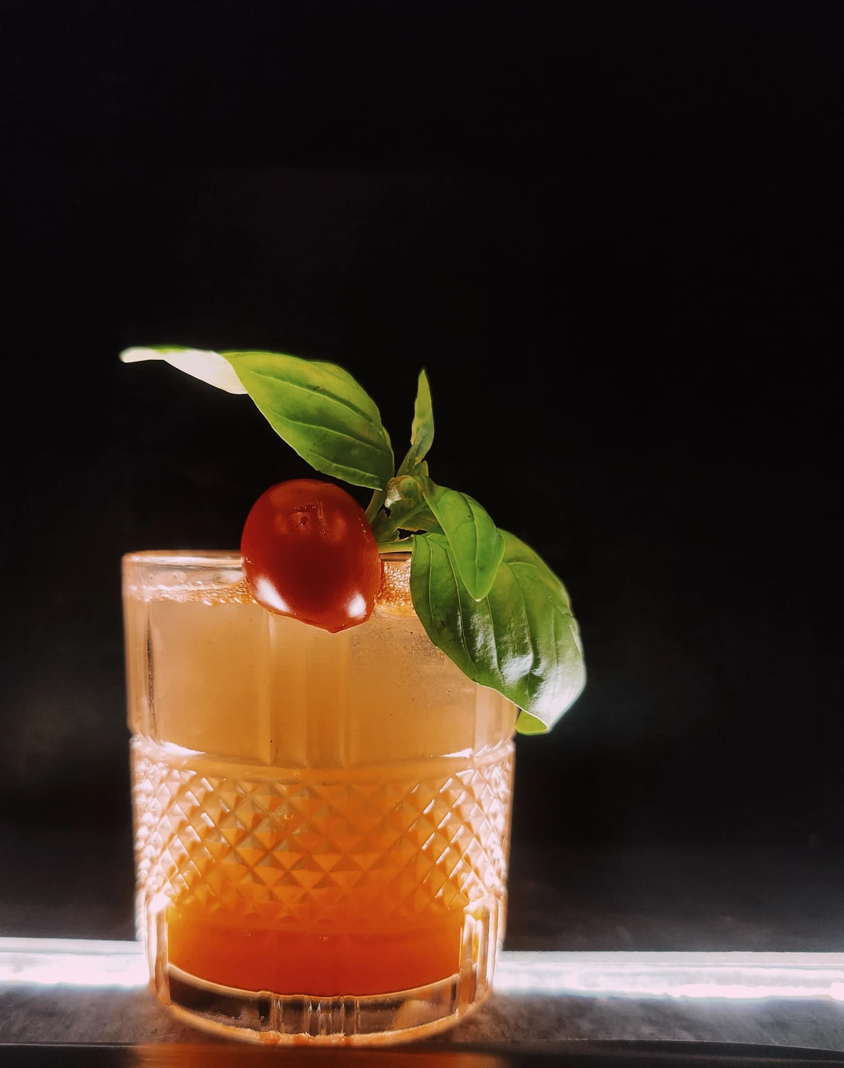 An orange cocktail garnished with basil and cherry tomato