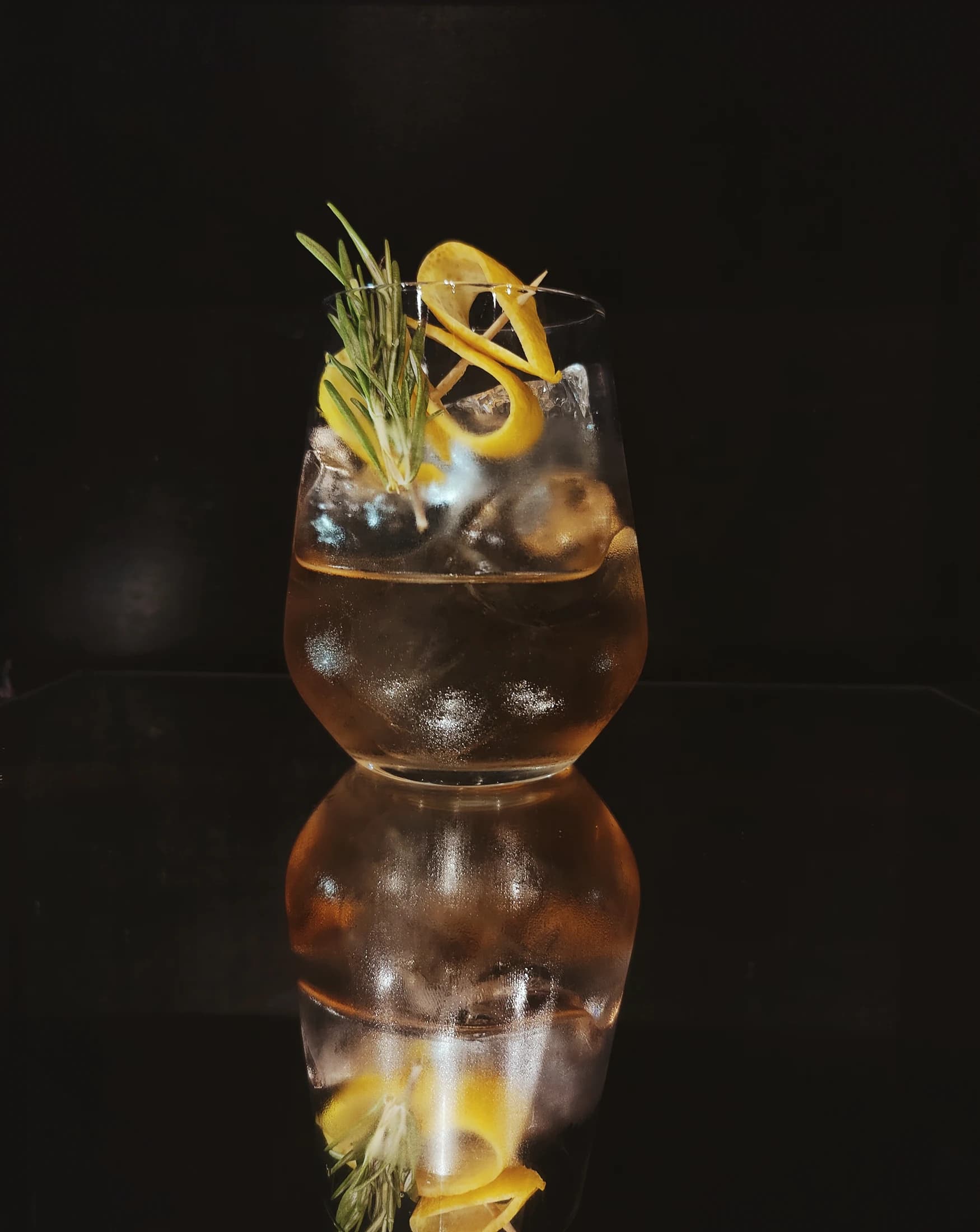 A gin and tonic with a rosemary and lemon twist, reflected on the bar