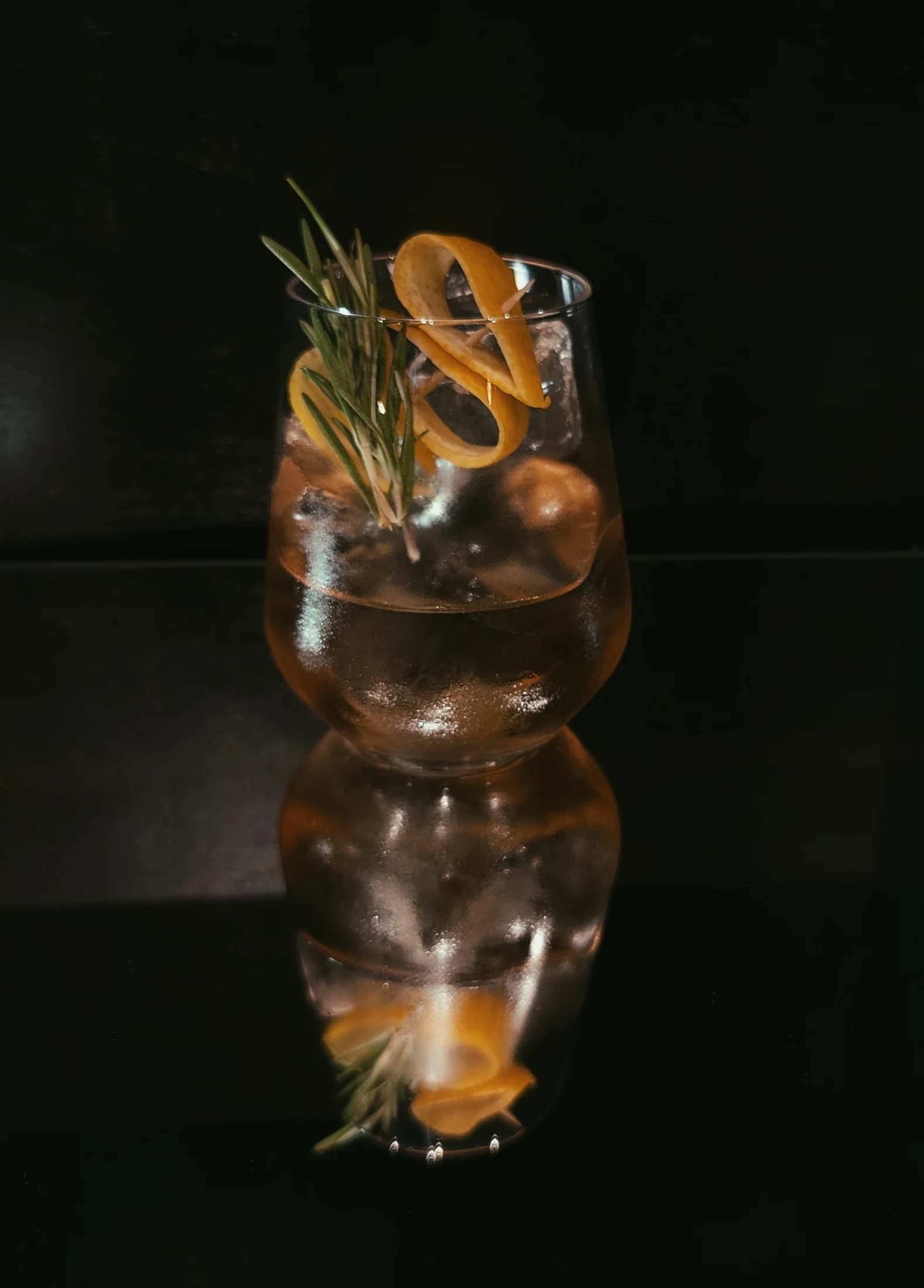 A gin cocktail reflected on the dark bar top