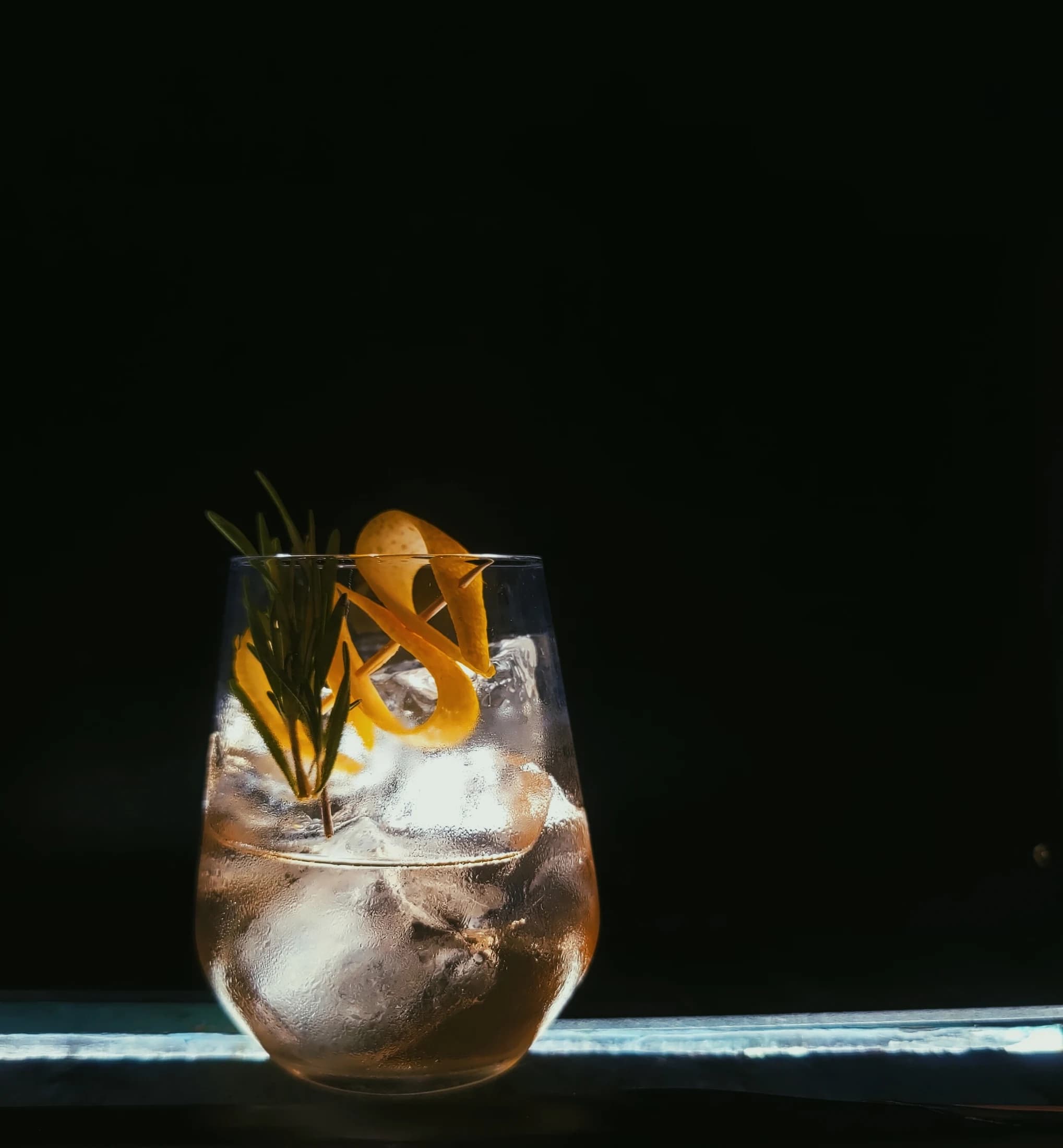 An amber cocktail with a rosemary and citrus garnish