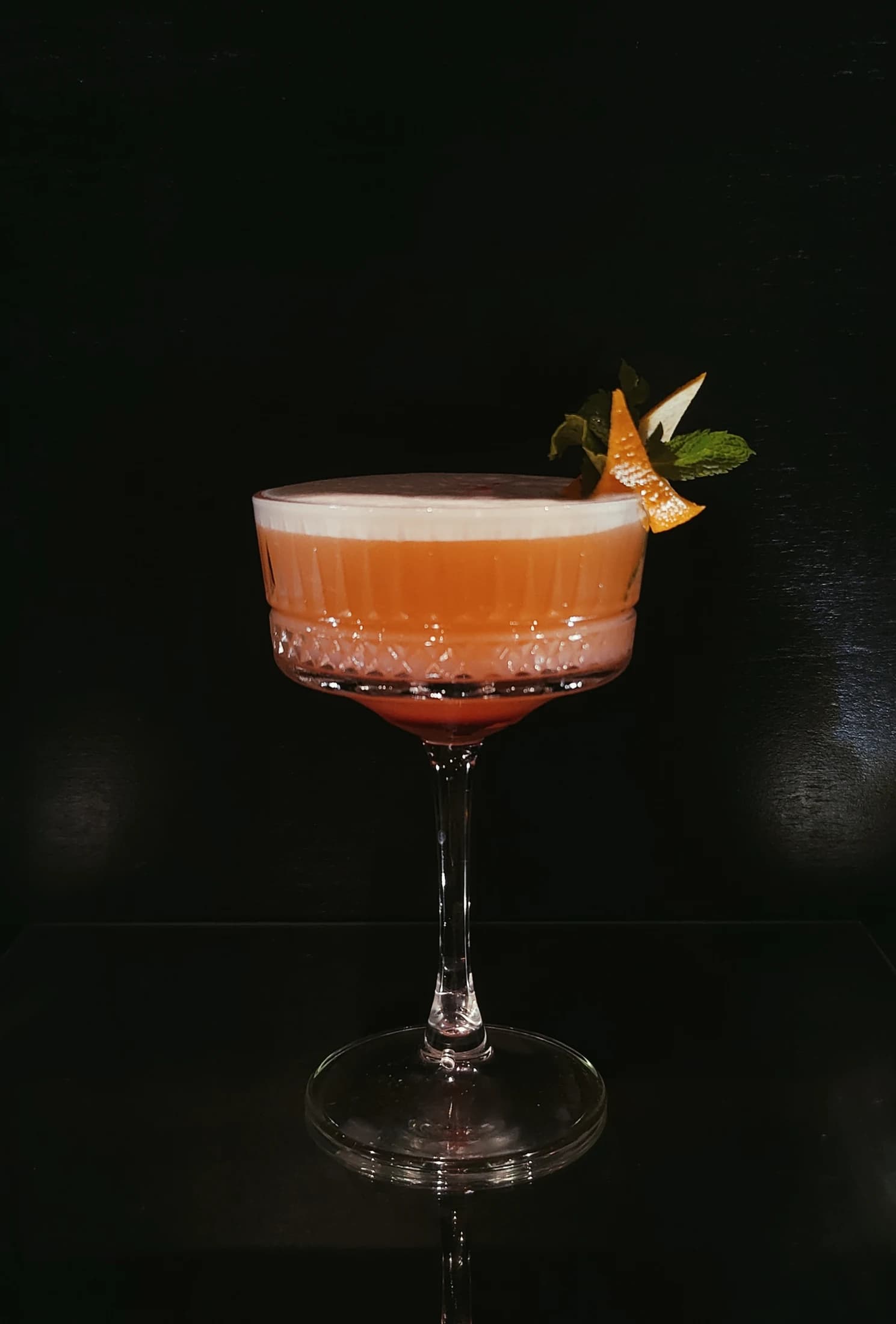 An orange cocktail in a coupe glass