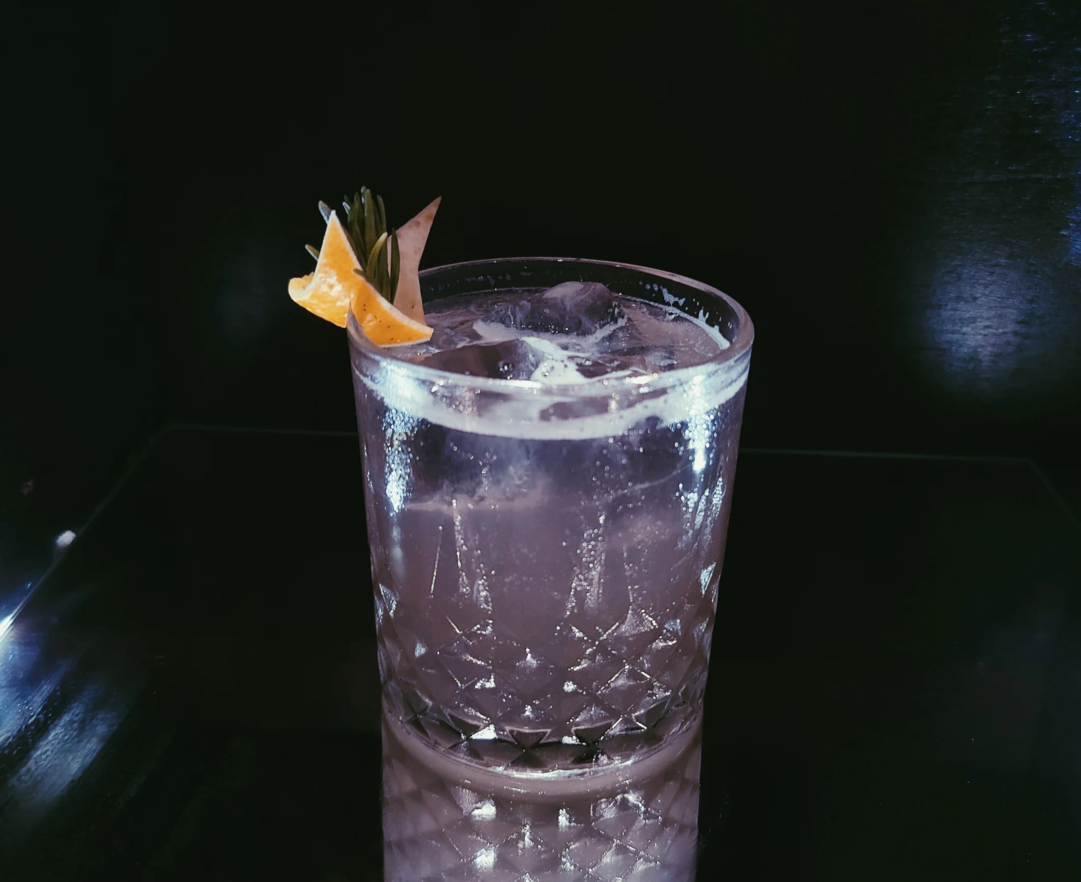 A sparkling lavender cocktail with an orange garnish