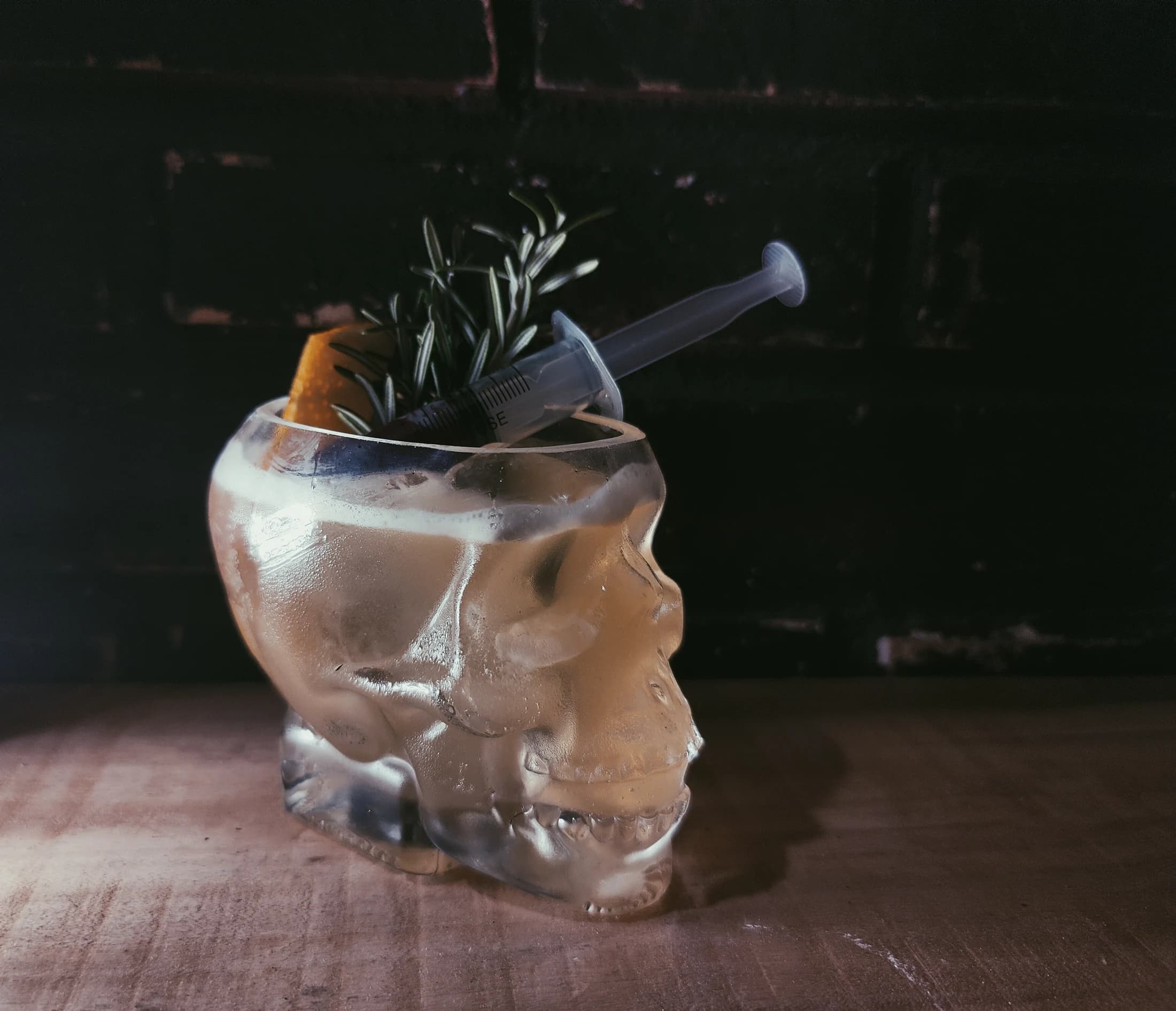 An amber cocktail in a skull-shaped mug with fresh herbs
