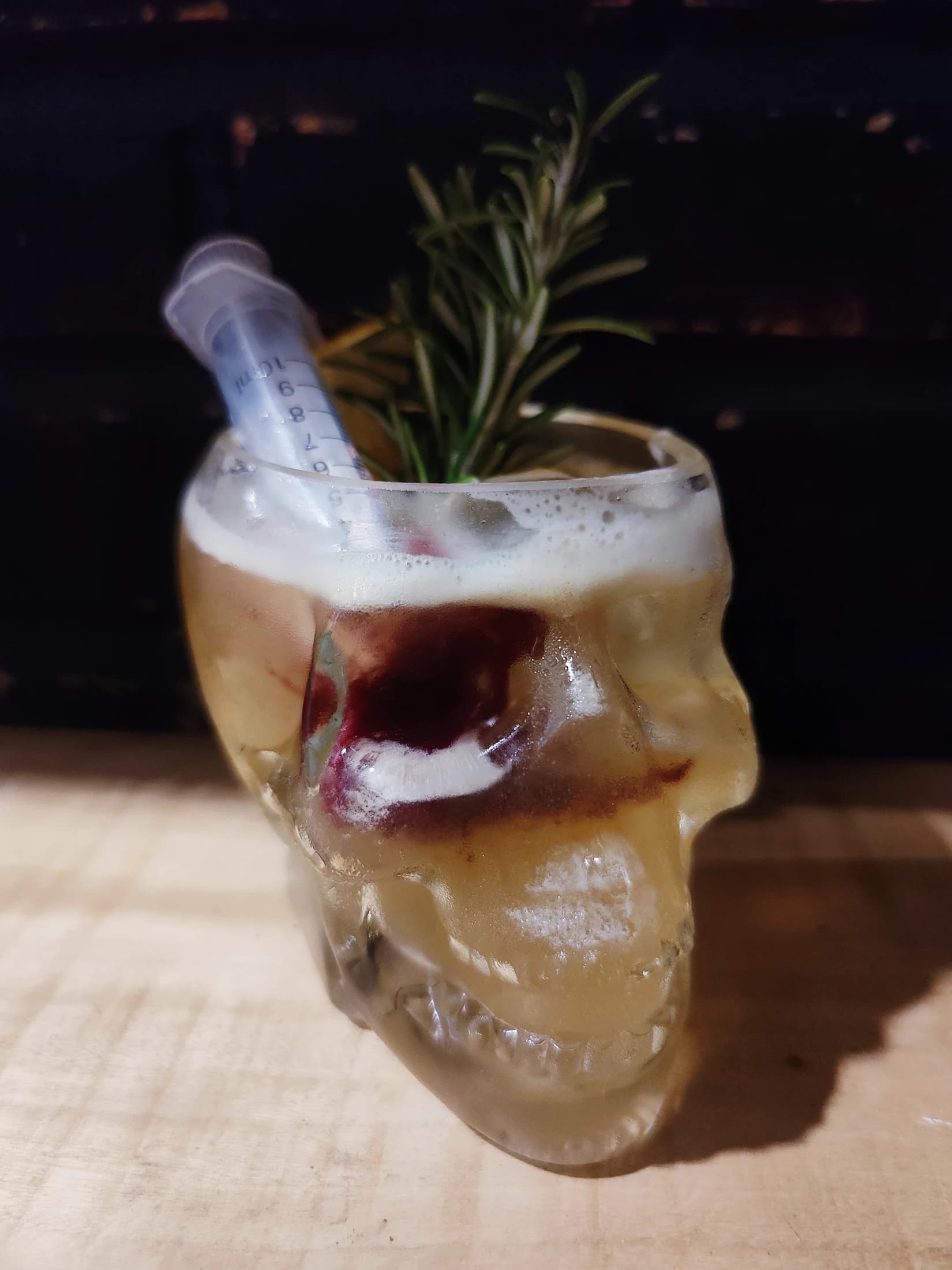 A frothy cocktail in a skull glass with a rosemary garnish