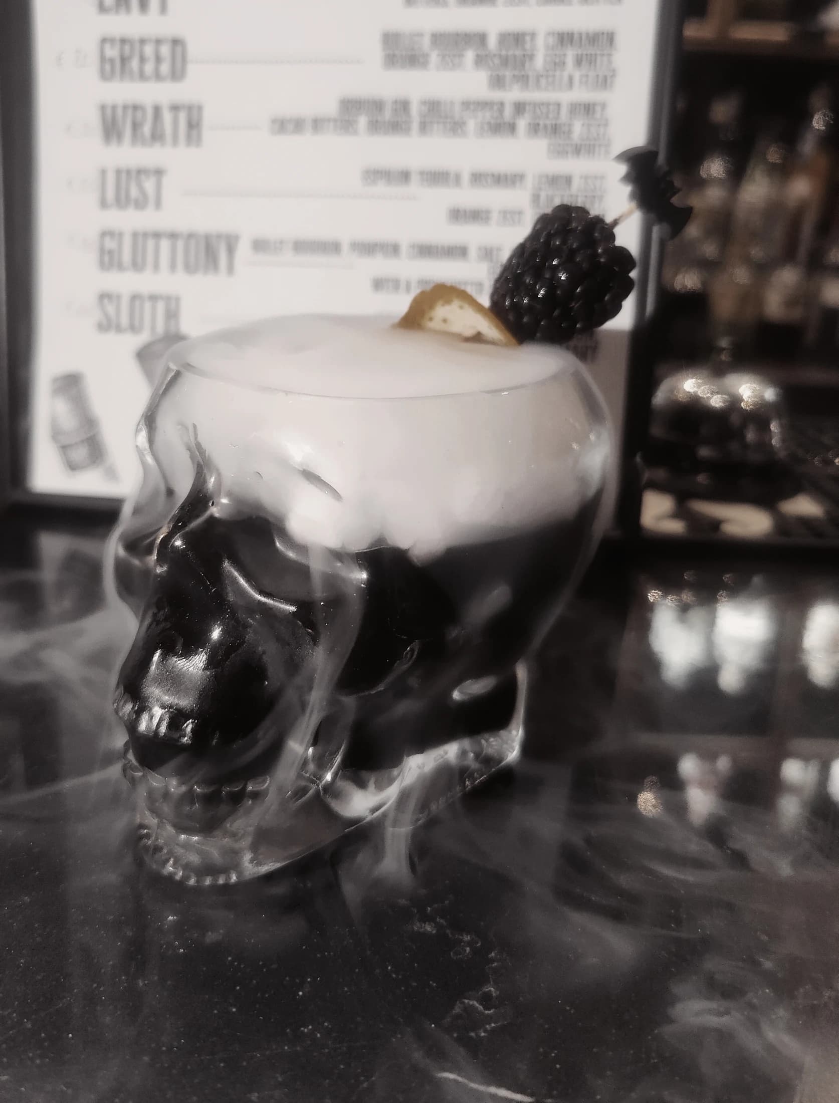 A dark cocktail in a skull glass garnished with blackberry