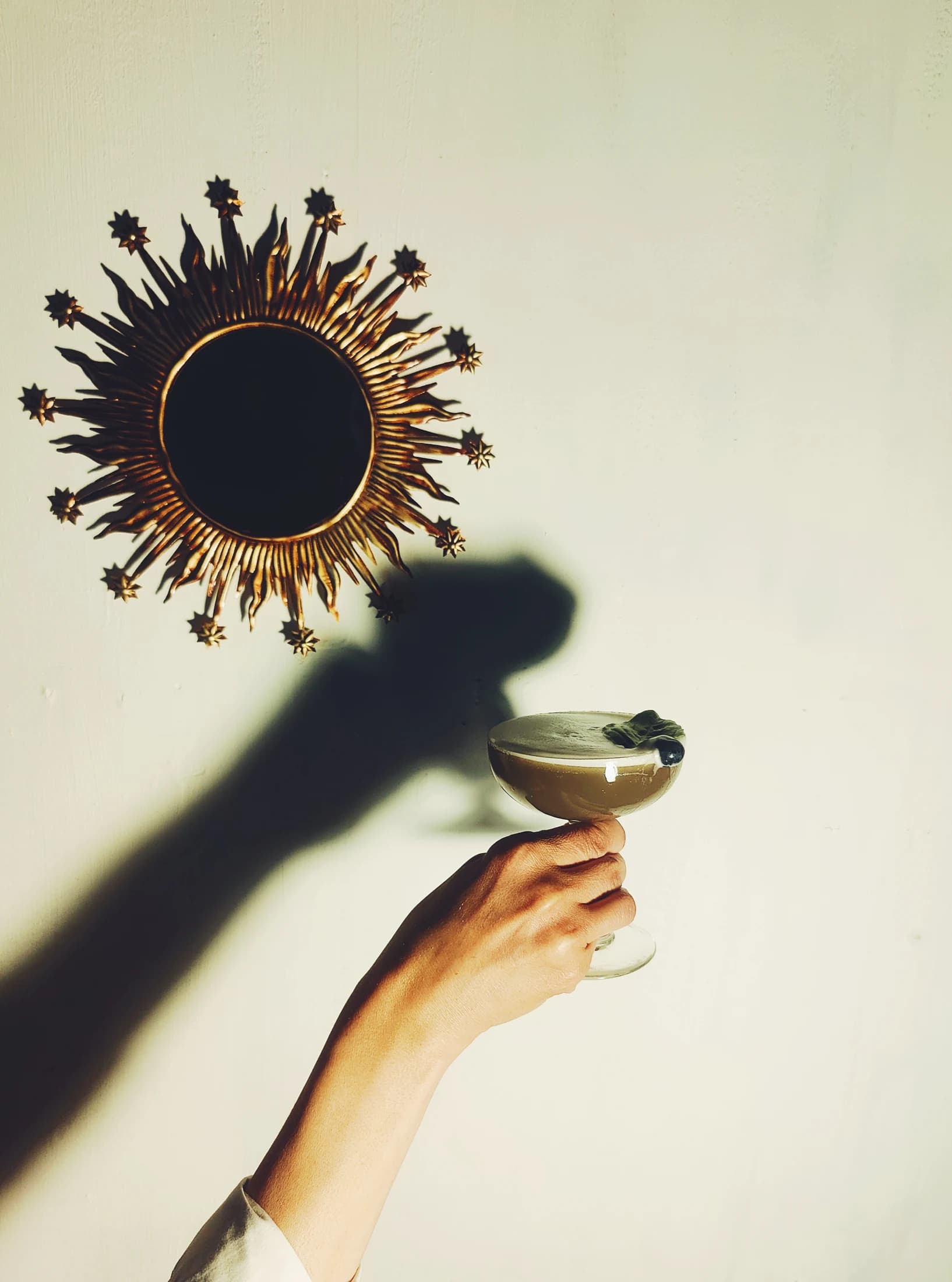 A martini held up beneath a sunburst mirror