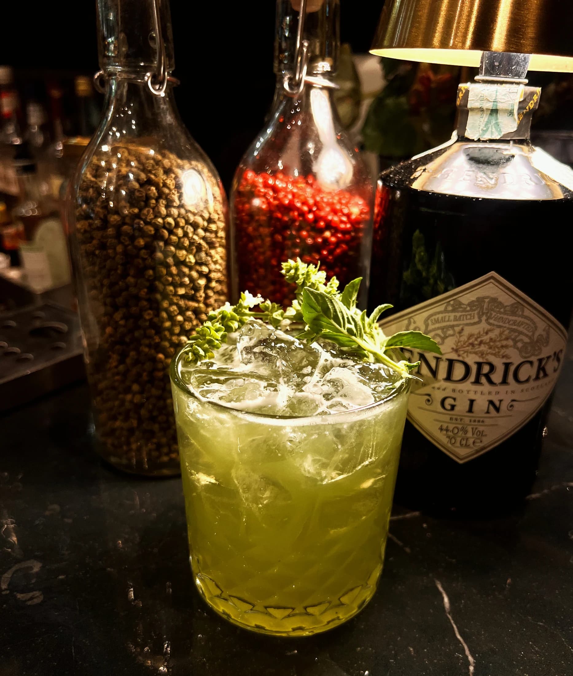 A green cocktail with a bottle of Hendrick's gin